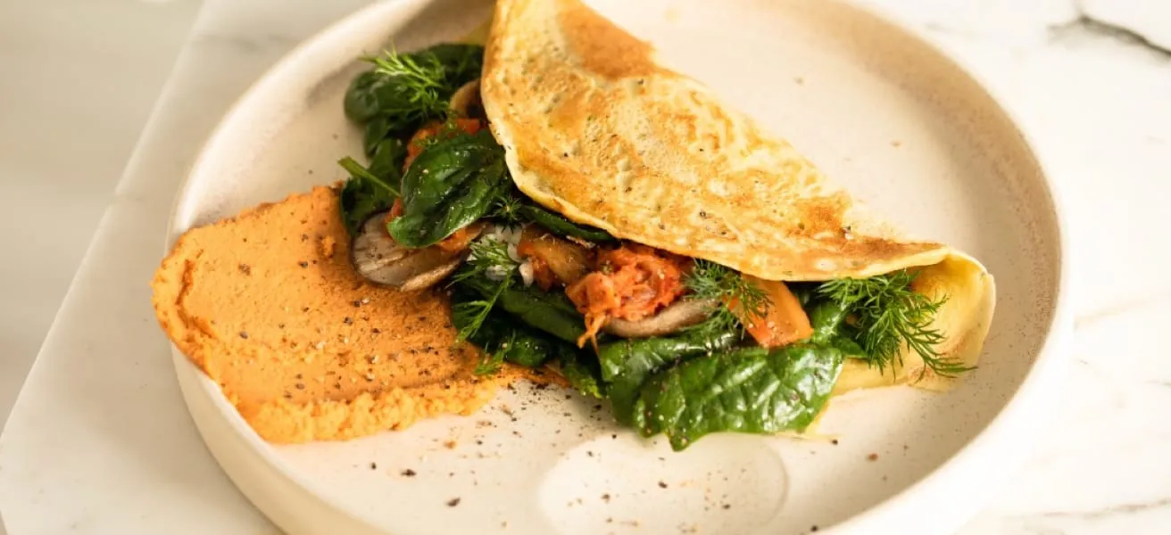 A folded omelette with spinach and greens on a white platter